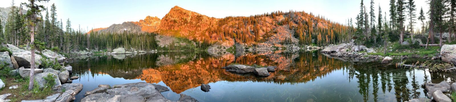 Panoramic mountain lake with orange rock peaks reflected in the water